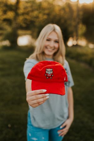 A young woman holding up a ball cap, proudly displaying her college of choice.