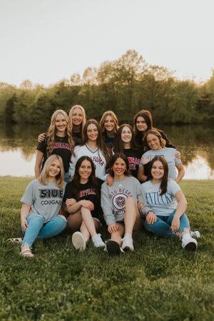 A group of high school senior girls wearing their chosen college apparel. They are proudly showing off where they will be attending school.