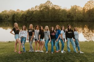 A group of high school senior girls wearing their chosen college apparel. They are holding hands in a line, outsite.