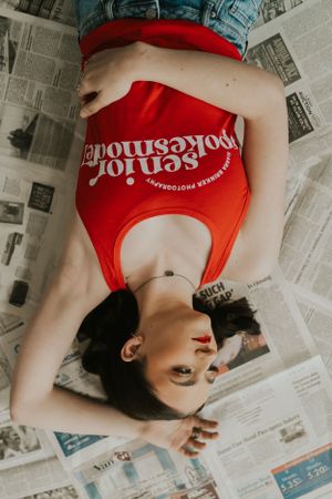 An artistic photo of a brunette young lady laying on the ground posing on top of newspapers.
