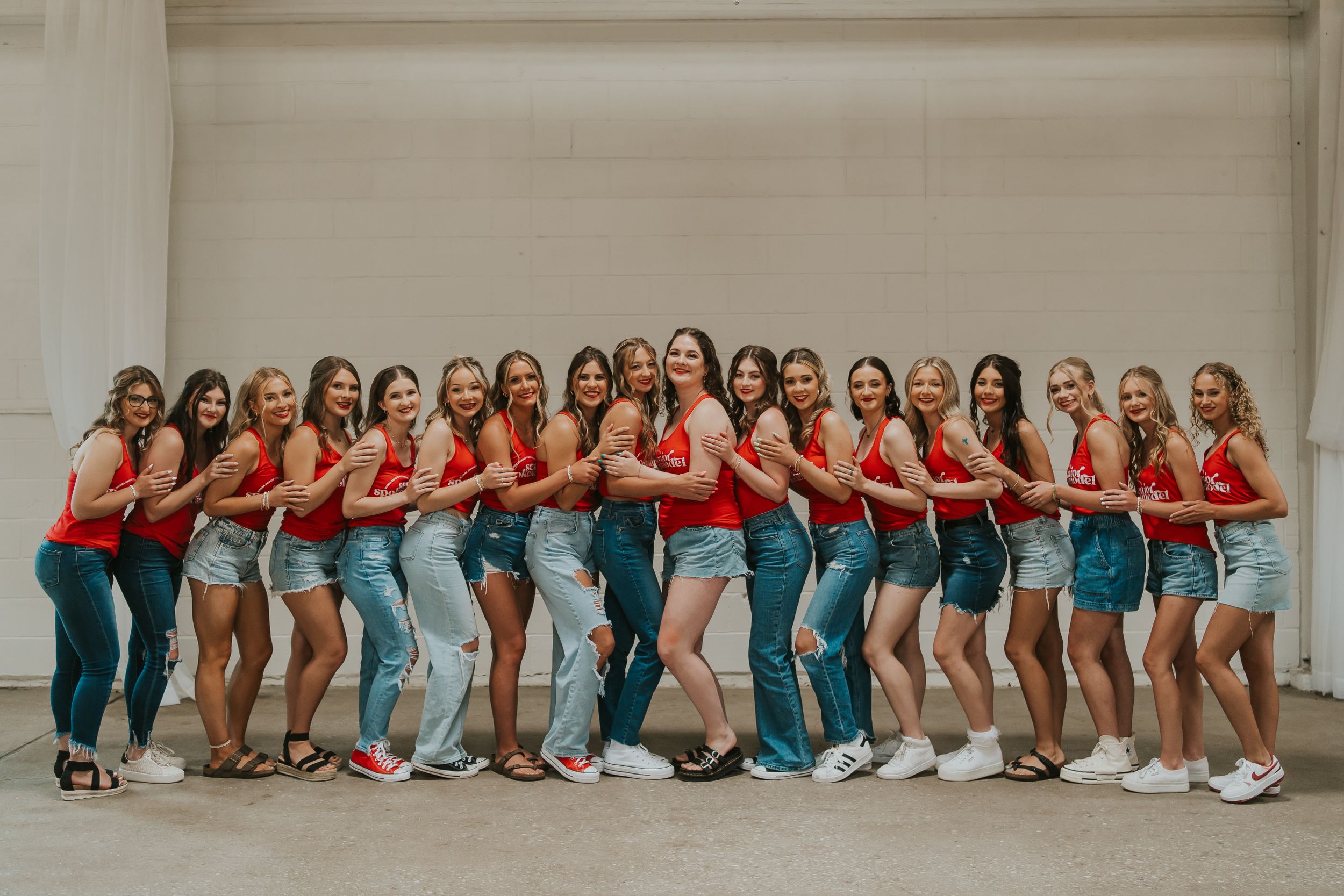 A group of high school seniors hugging each other in a line. They are all wearing matching red tank tops.