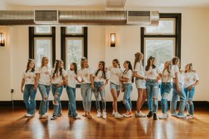 A group of high school senior girls wearing matching t-shirts. They are leaning on each other and holding hands while smiling and laughing.