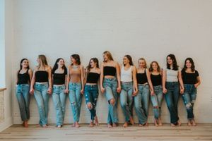 A group of friends leaning against the wall in a line. They are all wearing black or white tank tops with denim jeans, and are holding hands