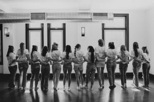A black and white photo of a group of young ladies with their arms around each other, looking at each other.