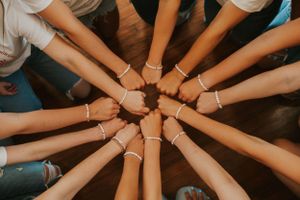 A group of high school senior girls wearing matching t-shirts showing off their matching bracelets by standing in a circle