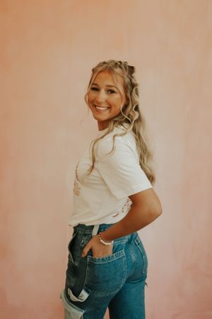A portrait of a high school senior with long blonde hair. She is looking over her shoulder and smiling at the camera.