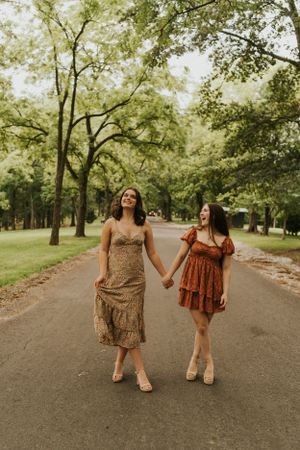 Two best friends standing in the middle of a country road, holding hands and laughing, while twirling their dresses.