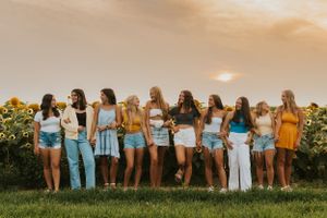 A group of high school friends standing in a sunflower patch at sunset. They are posing with one another and smiling at the camera.