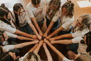 A group of high school senior girls wearing matching t-shirts showing off their matching bracelets by standing in a circle