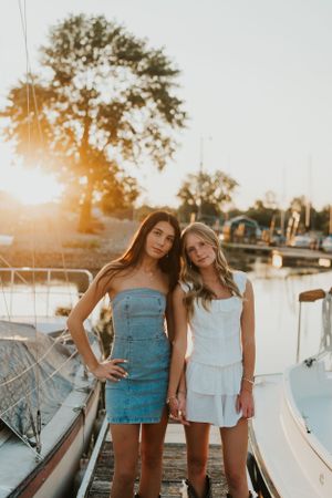 Two best friends at sunset on a boat dock, surrounded by the water and boats.