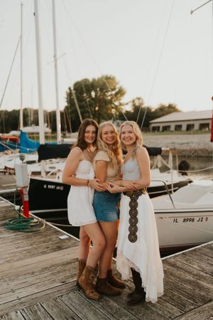 Three best friends at sunset on a boat dock, surrounded by the water and boats.