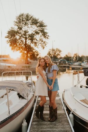 Two best friends at sunset on a boat dock, surrounded by the water and boats.