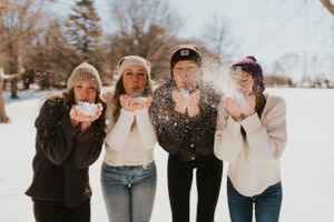 A group of teenagers holding snow in their hands. Some of the snow is blowing around.
