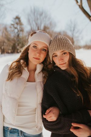 Two young women in the snow, bundled up and leaning on each other in a pose for a photograph.