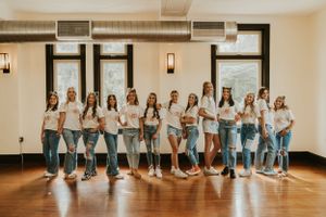 A group of high school senior girls wearing matching t-shirts, posing seriously for the camera in a straight line.