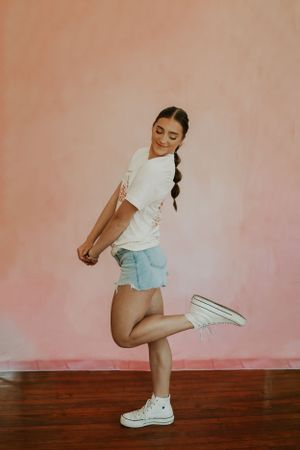 A high school senior portrait of a girl with a long brunette braid posing in front of a pink backdrop.
