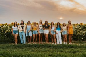 A group of best friends at a sunflower field at sunset. They are wearing denim, yellow and white clothing and are holding hands while posing