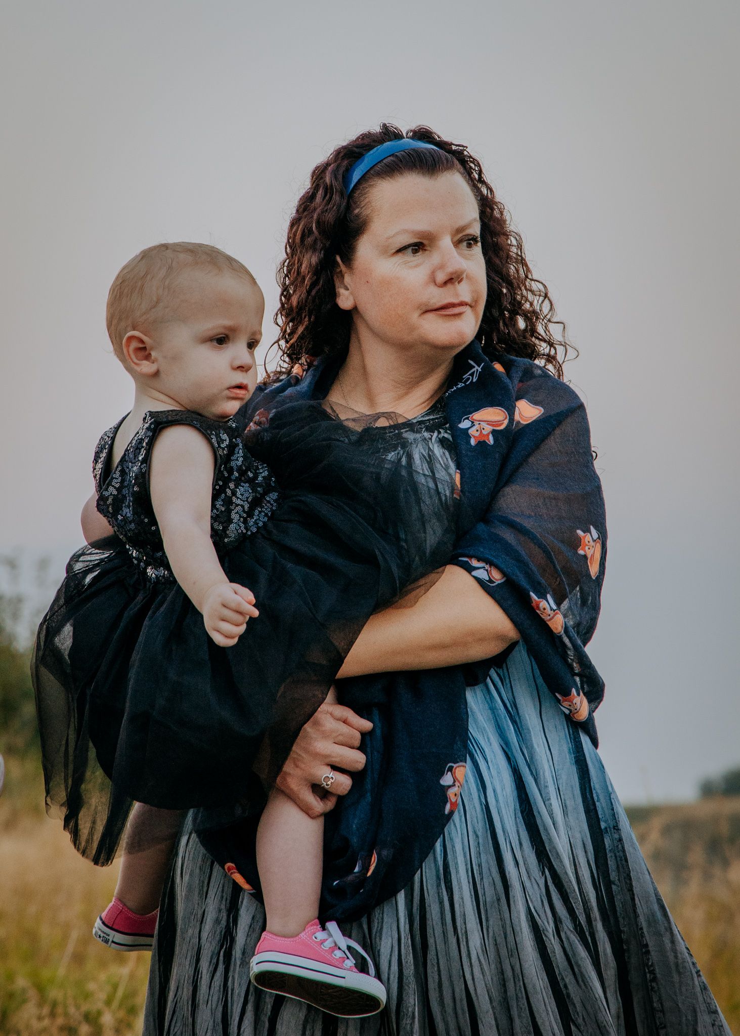 Parent carrying young child in navy formal wear against rural backdrop.
