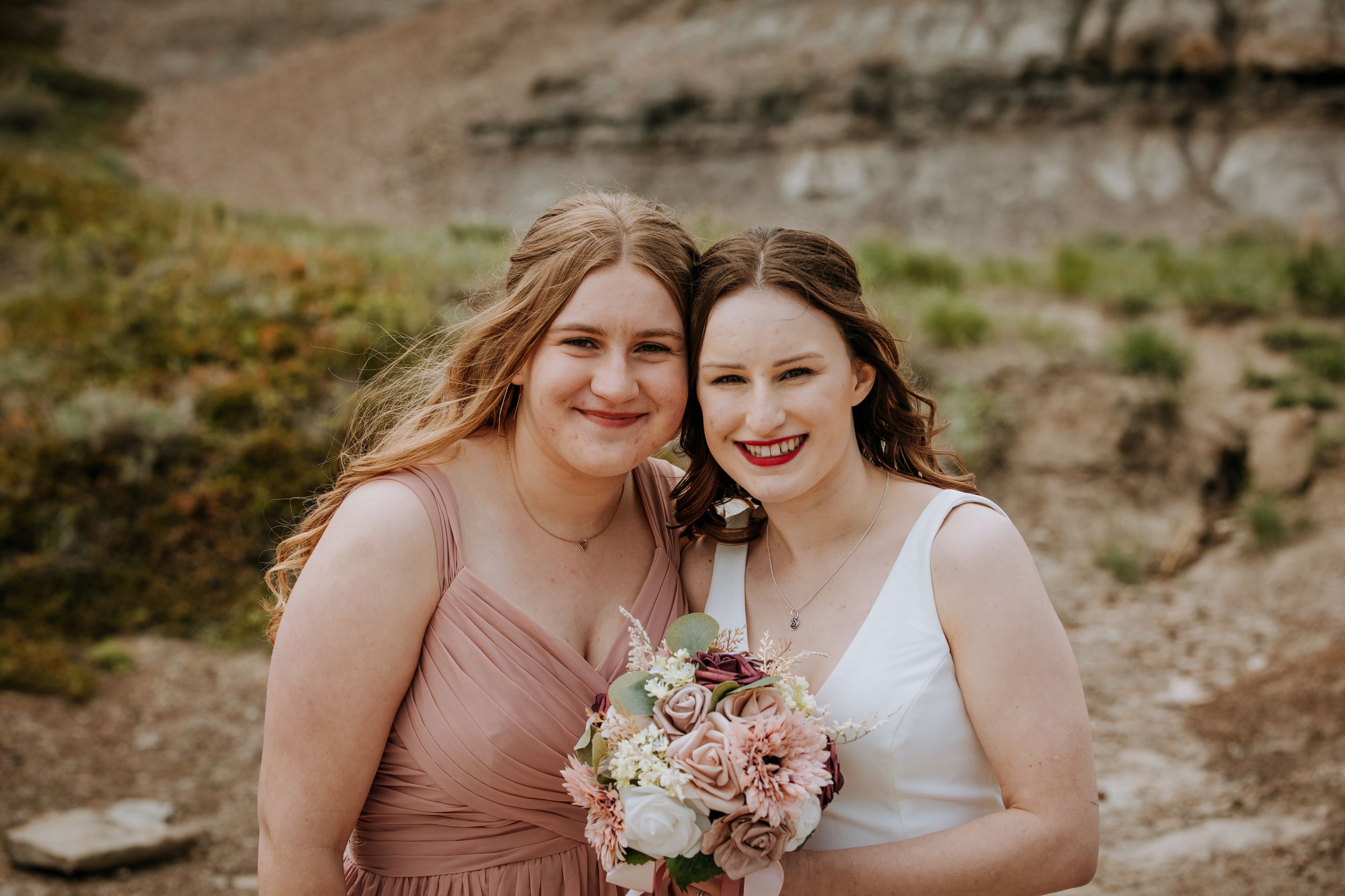 Two figures in pink and white dresses hold bouquet during outdoor photo session.