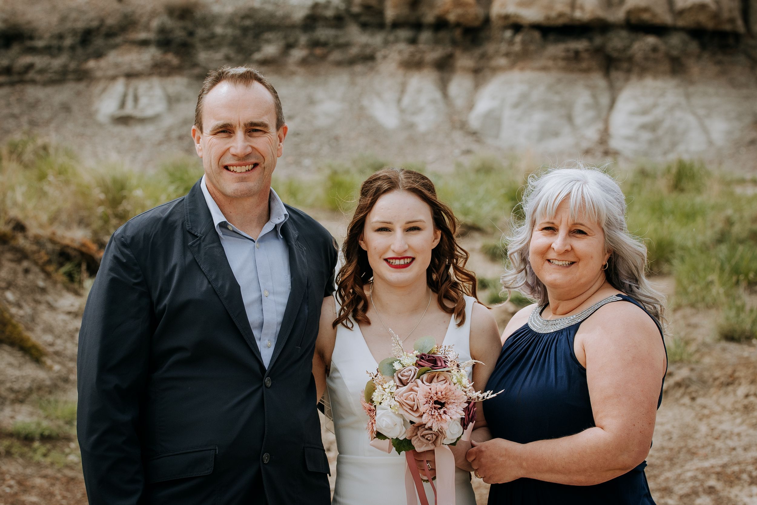 Group of three poses with bouquet against rocky mountain backdrop.