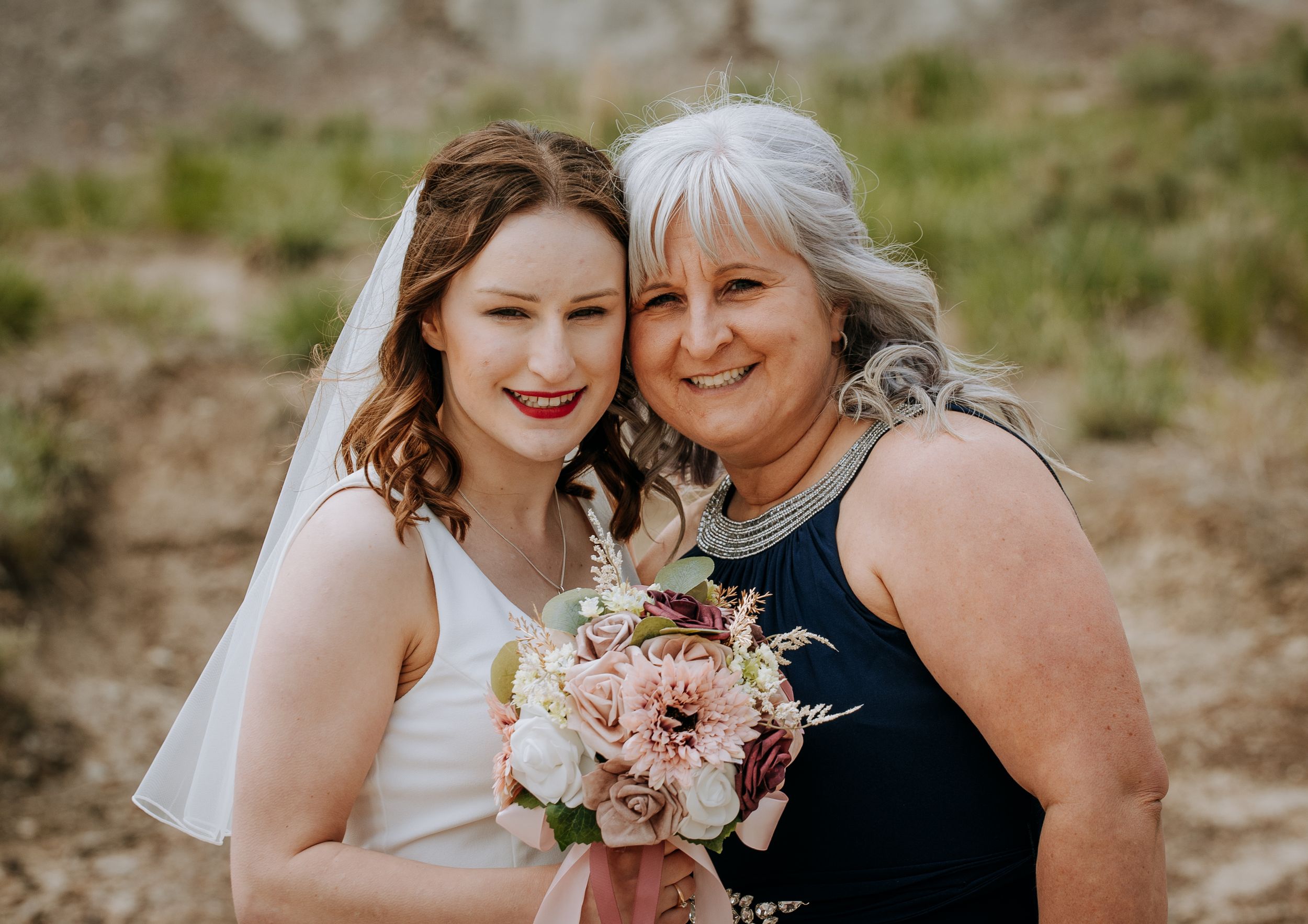 Two people share joyful moment while holding pink floral bouquet outdoors.