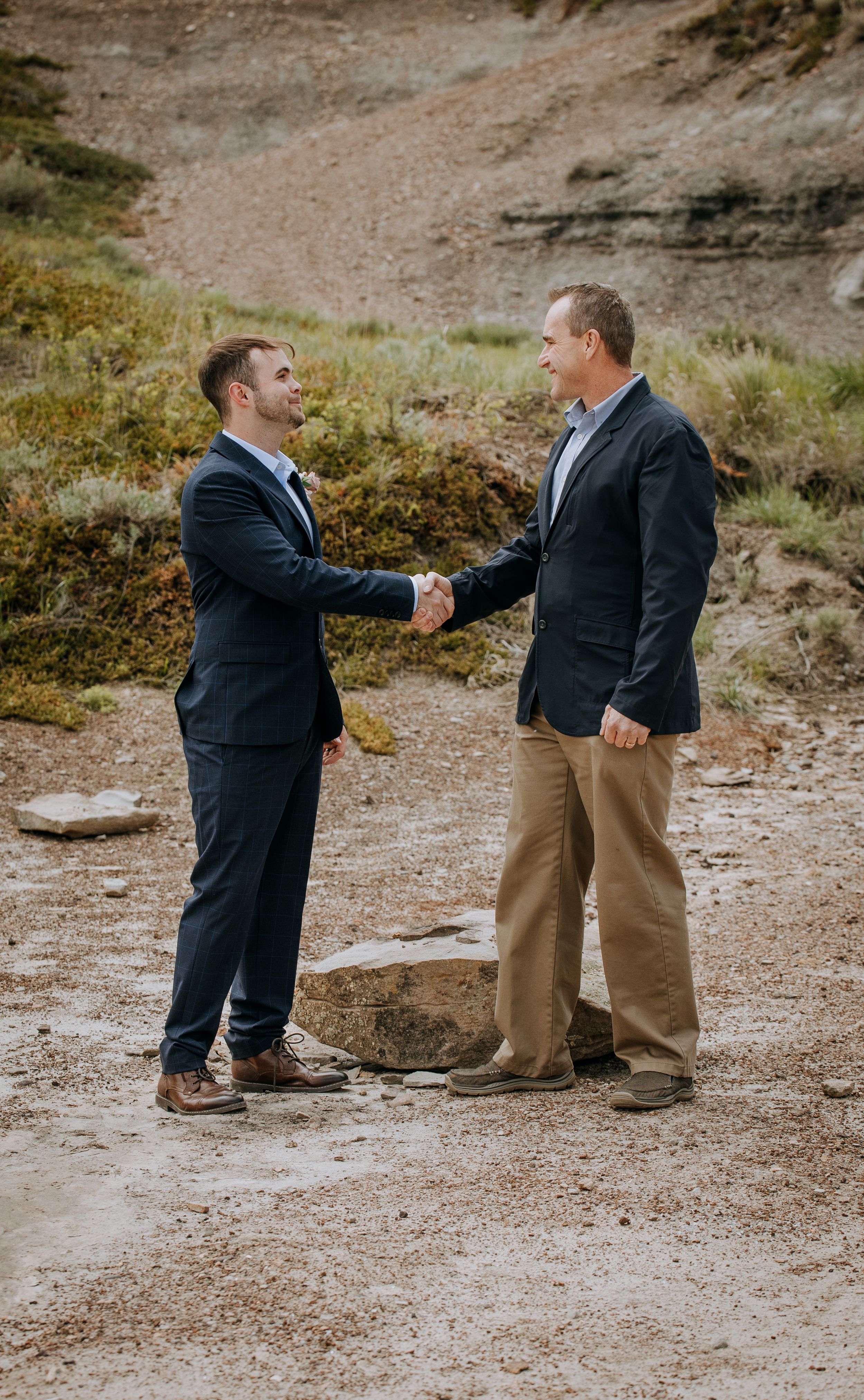 Two people shake hands on rocky terrain during outdoor photo session.