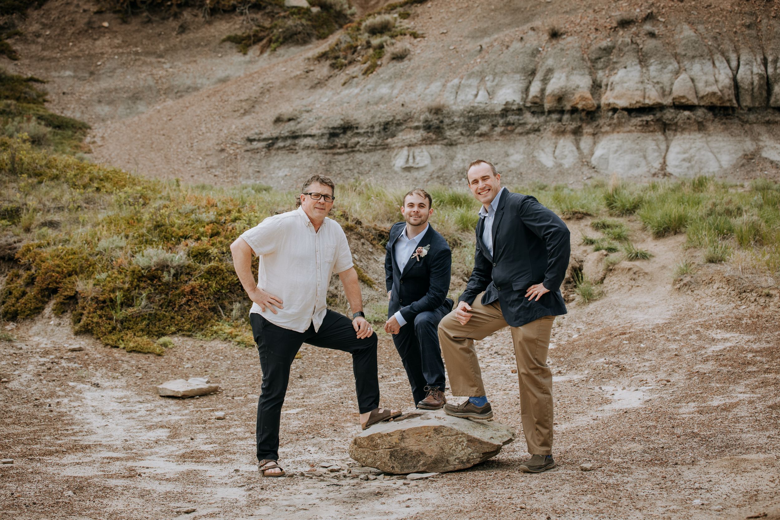 Three people pose playfully on rock formation in desert setting.