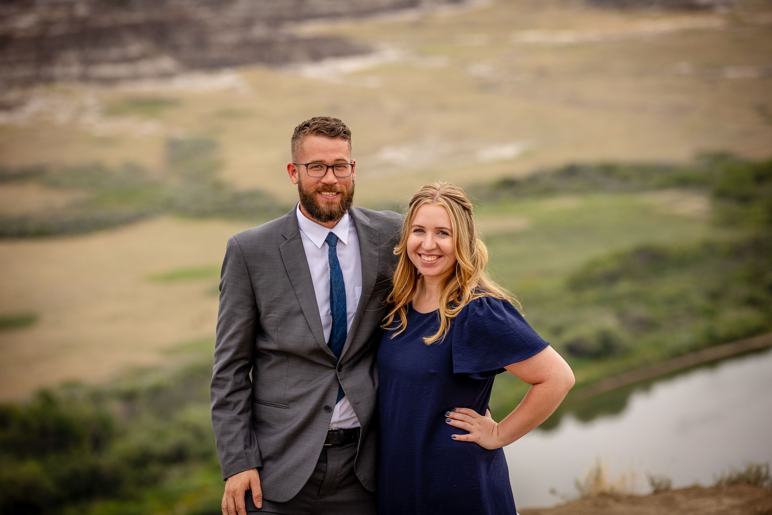 A couple poses together against a scenic mountain backdrop with a river winding below.