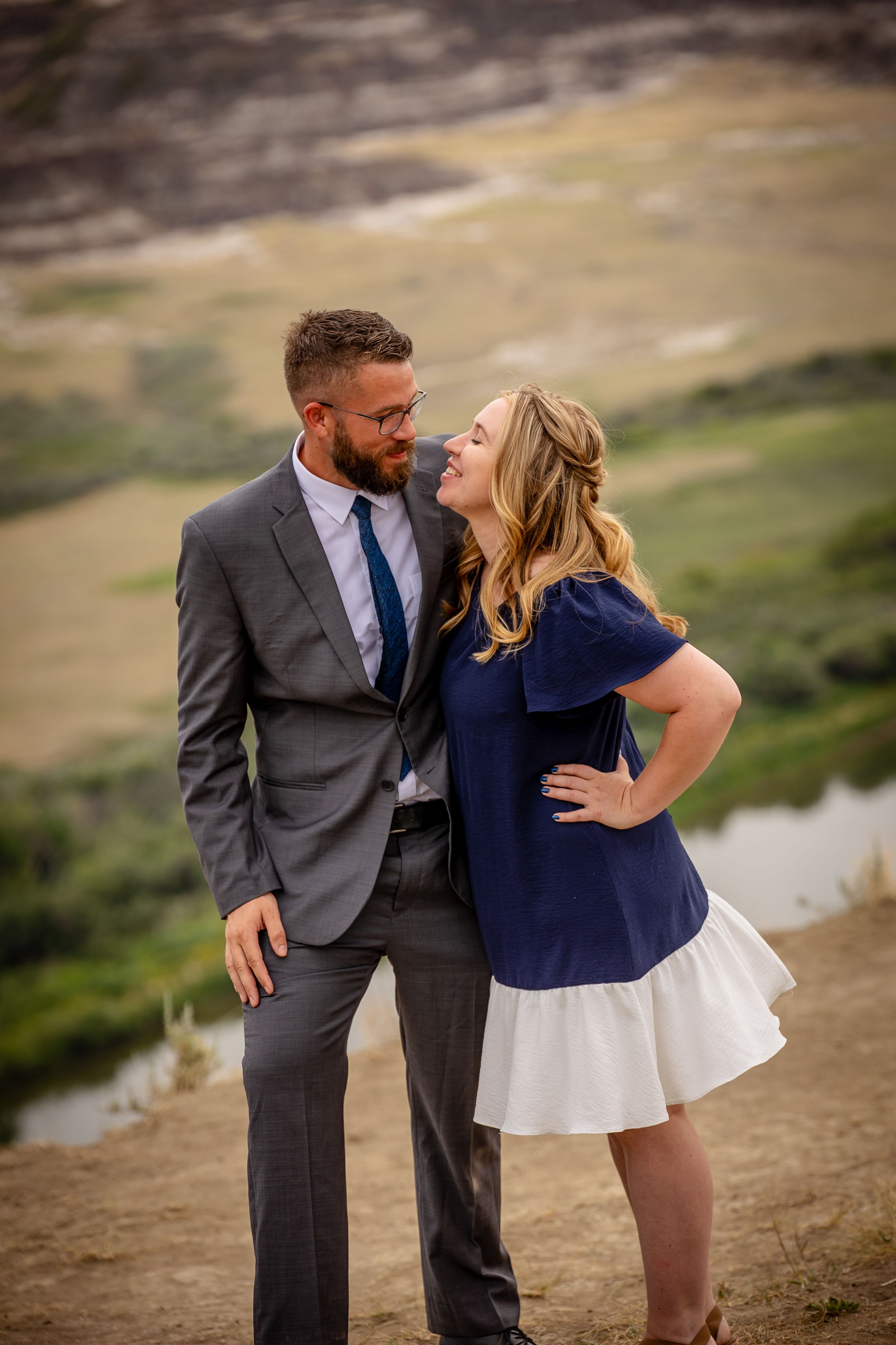 Romantic couple shares a playful moment on a hillside overlooking a valley.
