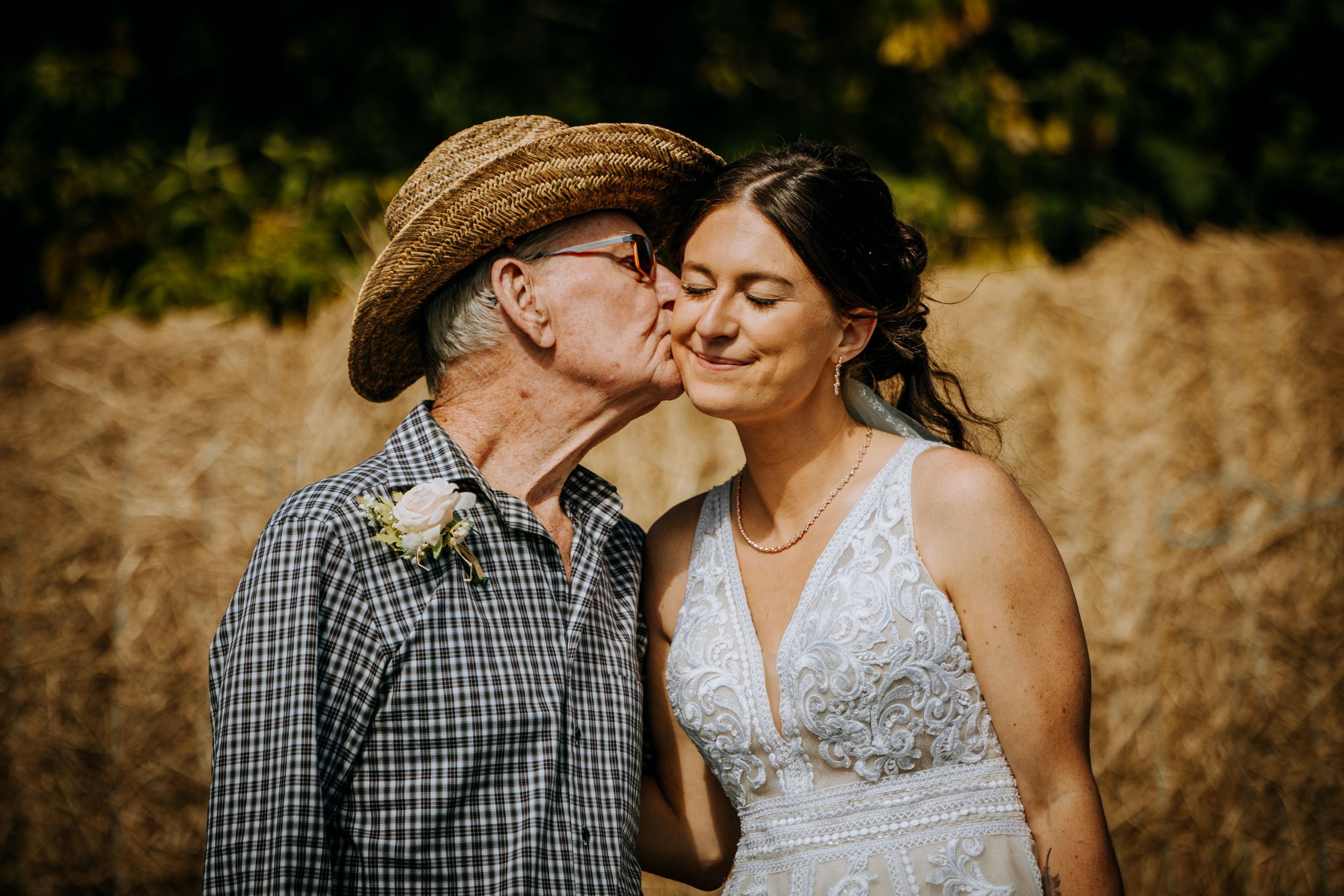 Tender moment captured against rustic hay bale backdrop during wedding celebration.