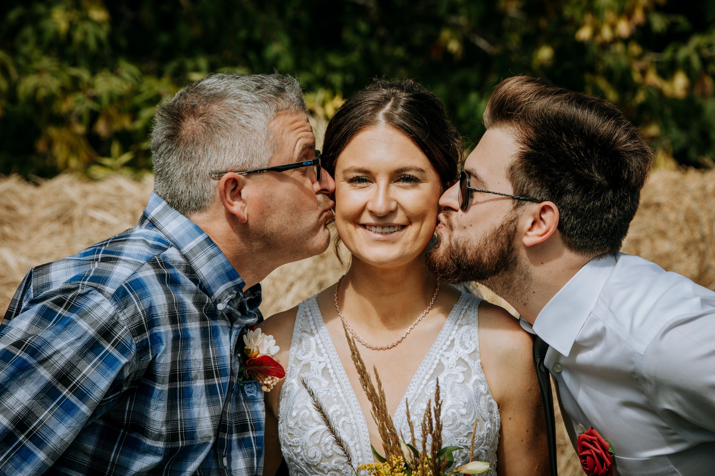 Joyful wedding portrait against hay bale backdrop with warm autumn lighting.