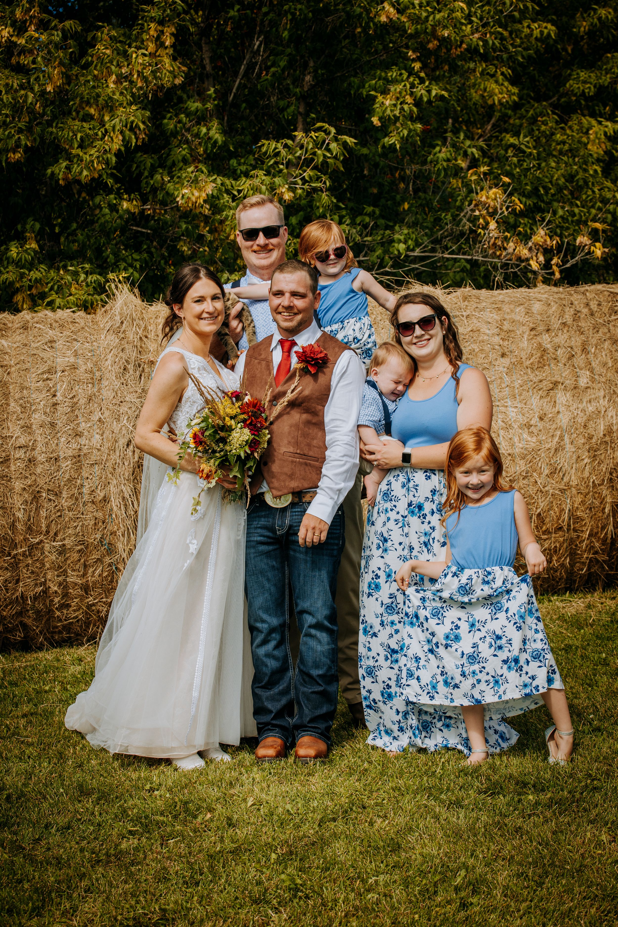 Wedding party poses together outdoors with colorful bouquet and coordinating blue and floral dresses.
