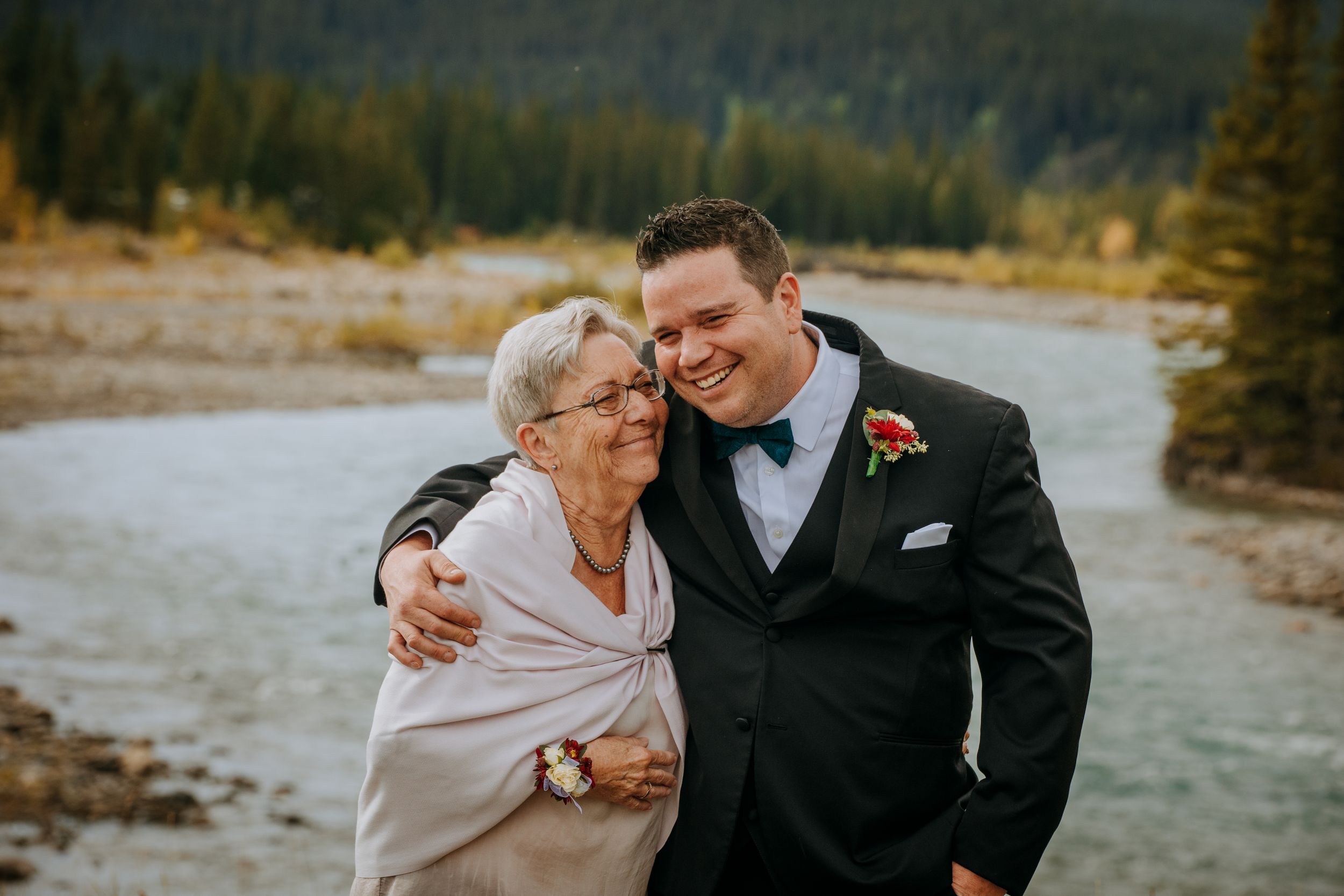 Sweet moment shared on mountainous riverside during wedding celebration.