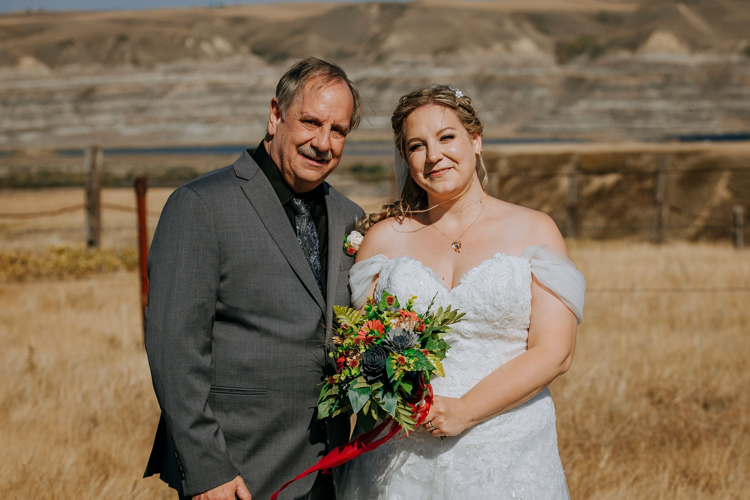 Wedding couple poses in formal attire with colorful bouquet against desert hills.