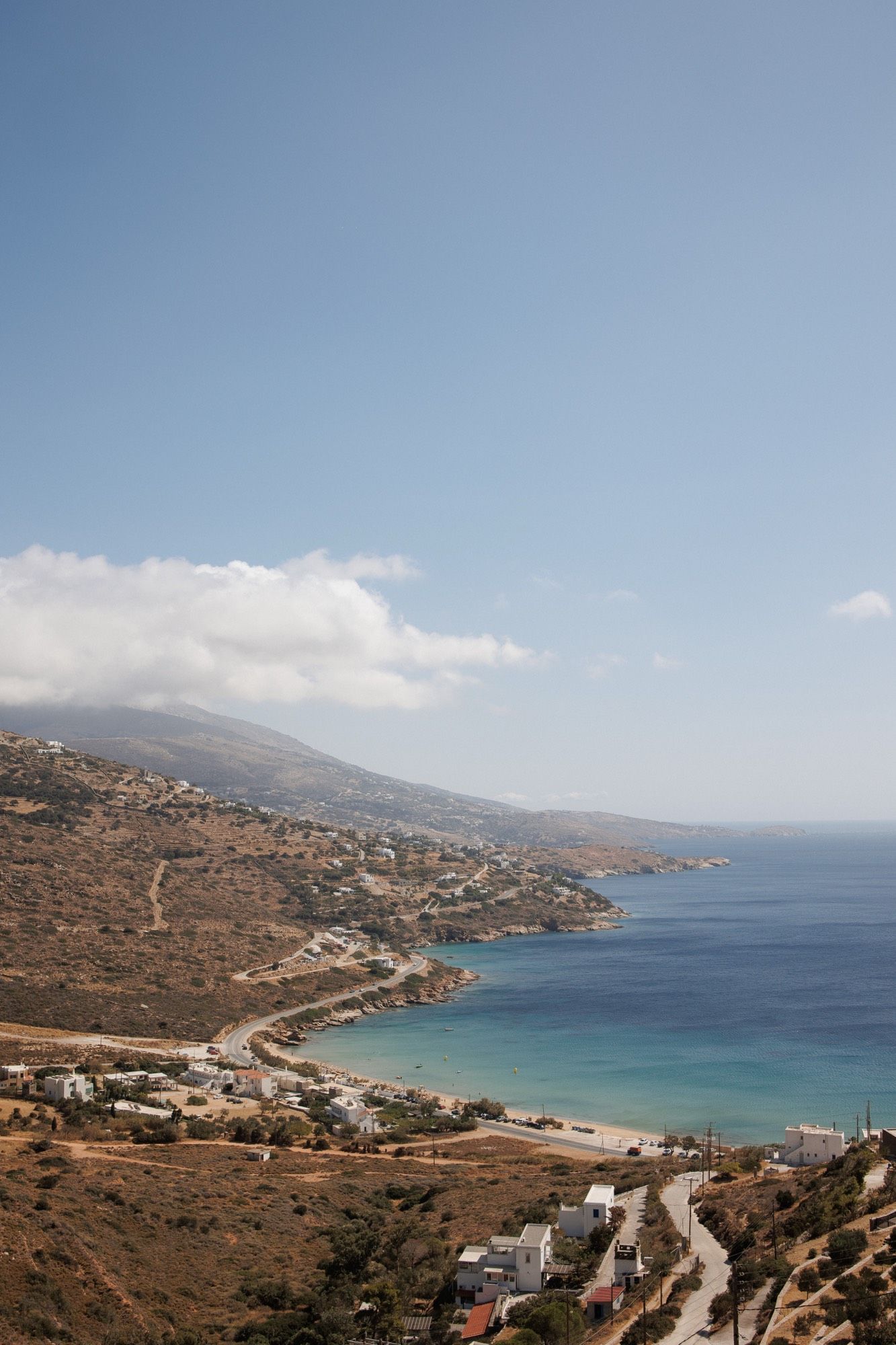 Panoramic view of a winding coastal road along a Mediterranean bay with turquoise waters and rugged hillsides.