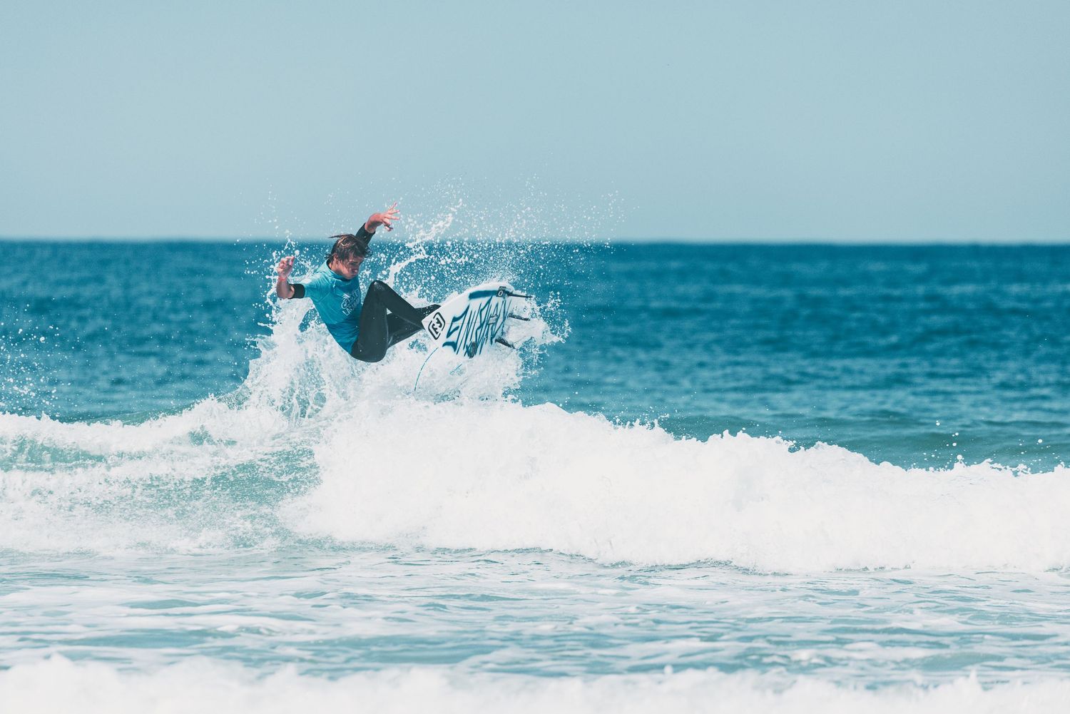 Un surfeur effectue une manœuvre aérienne au-dessus d'une vague océanique qui se brise par une journée ensoleillée.