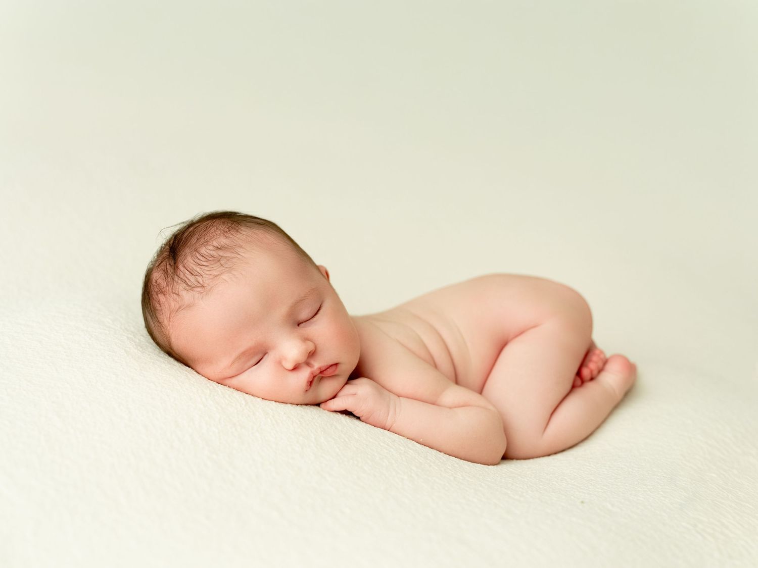 A smiling parent in a white shirt holds and lovingly gazes at their newborn baby wrapped in a cream blanket.