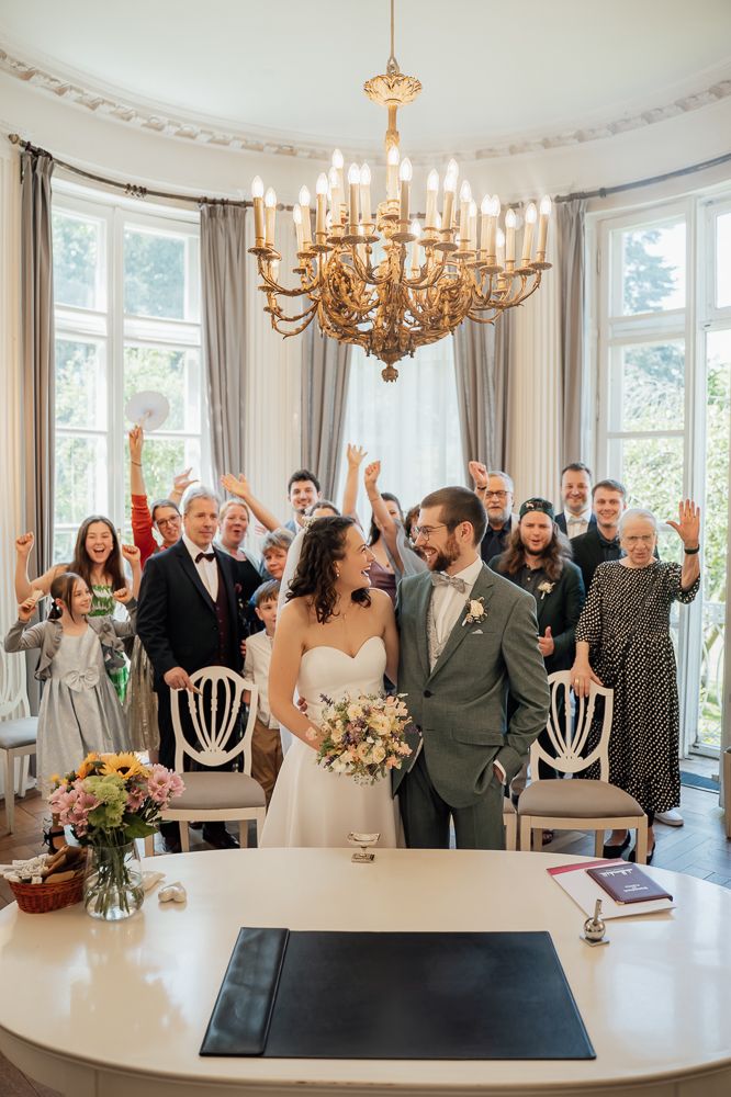 Joyful celebration sequence during an elegant wedding ceremony in a bright room with chandeliers and large windows.
