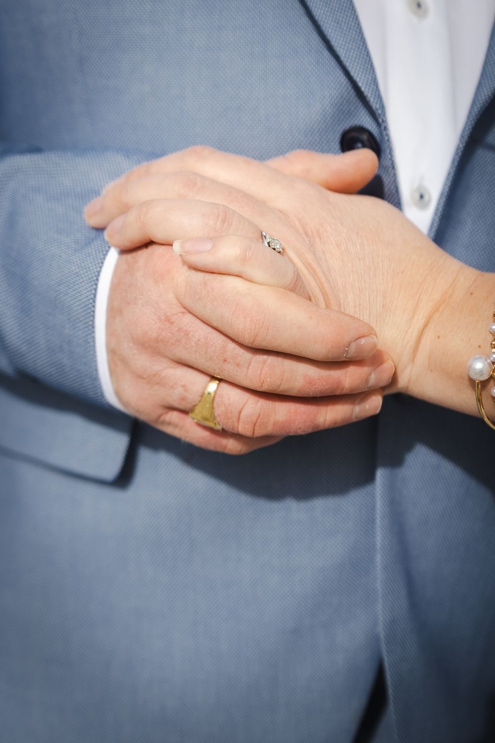 Close-up view of hands wearing gold wedding rings against a gray suit background.