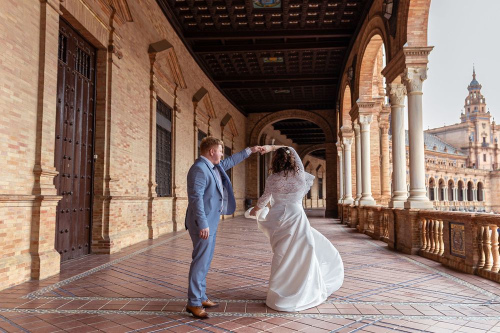 A panoramic view of a bride and groom walking through the ornate colonnade at Plaza de Espana in Seville, Spain.