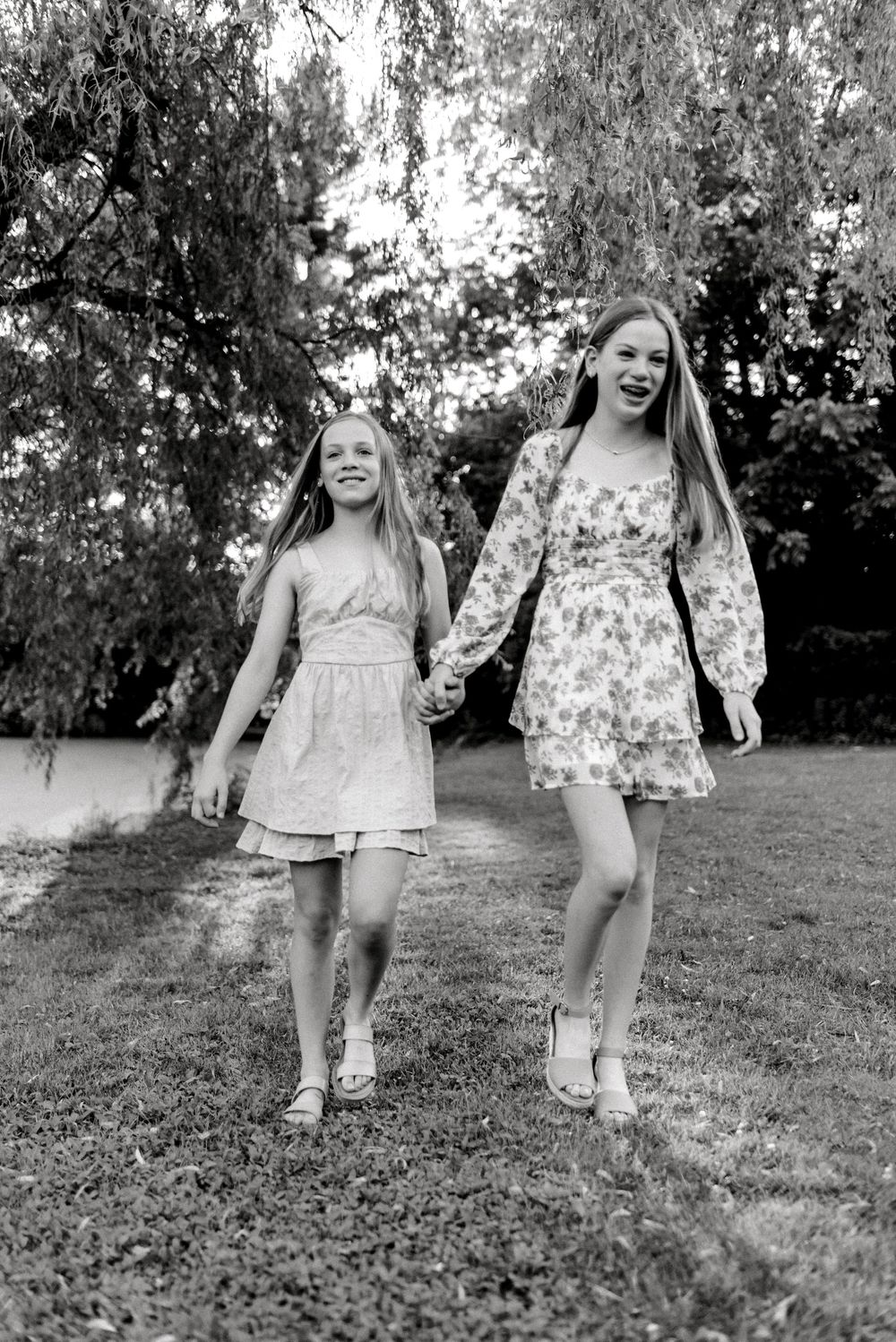 Sisters walking and holding hands under willow tree in Pittsburgh, PA