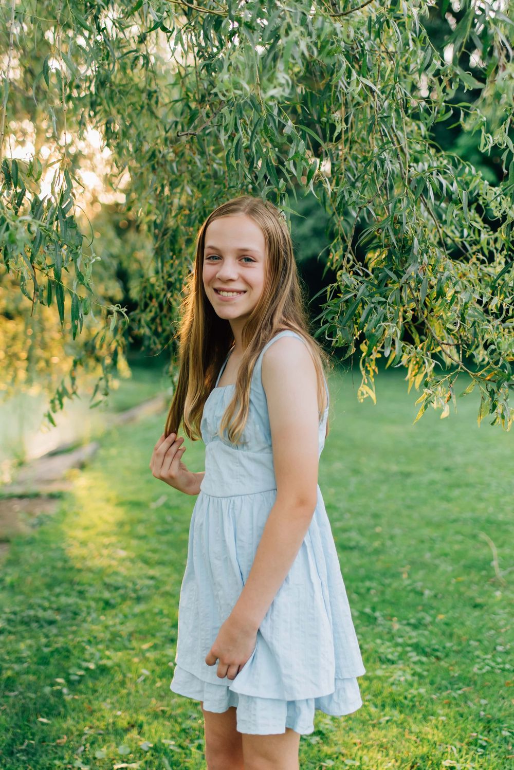 Young girl smiling under willow tree at golden hour