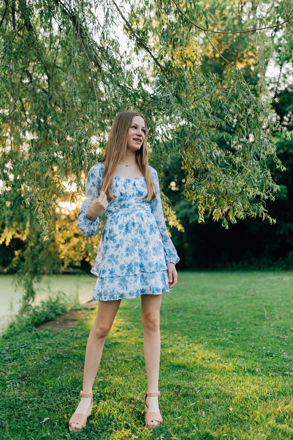 Young girl standing under willow tree in golden hour sunlight