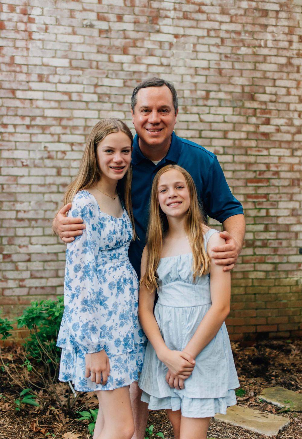 Dad and daughters smiling in front of brick wall in Pittsburgh, PA