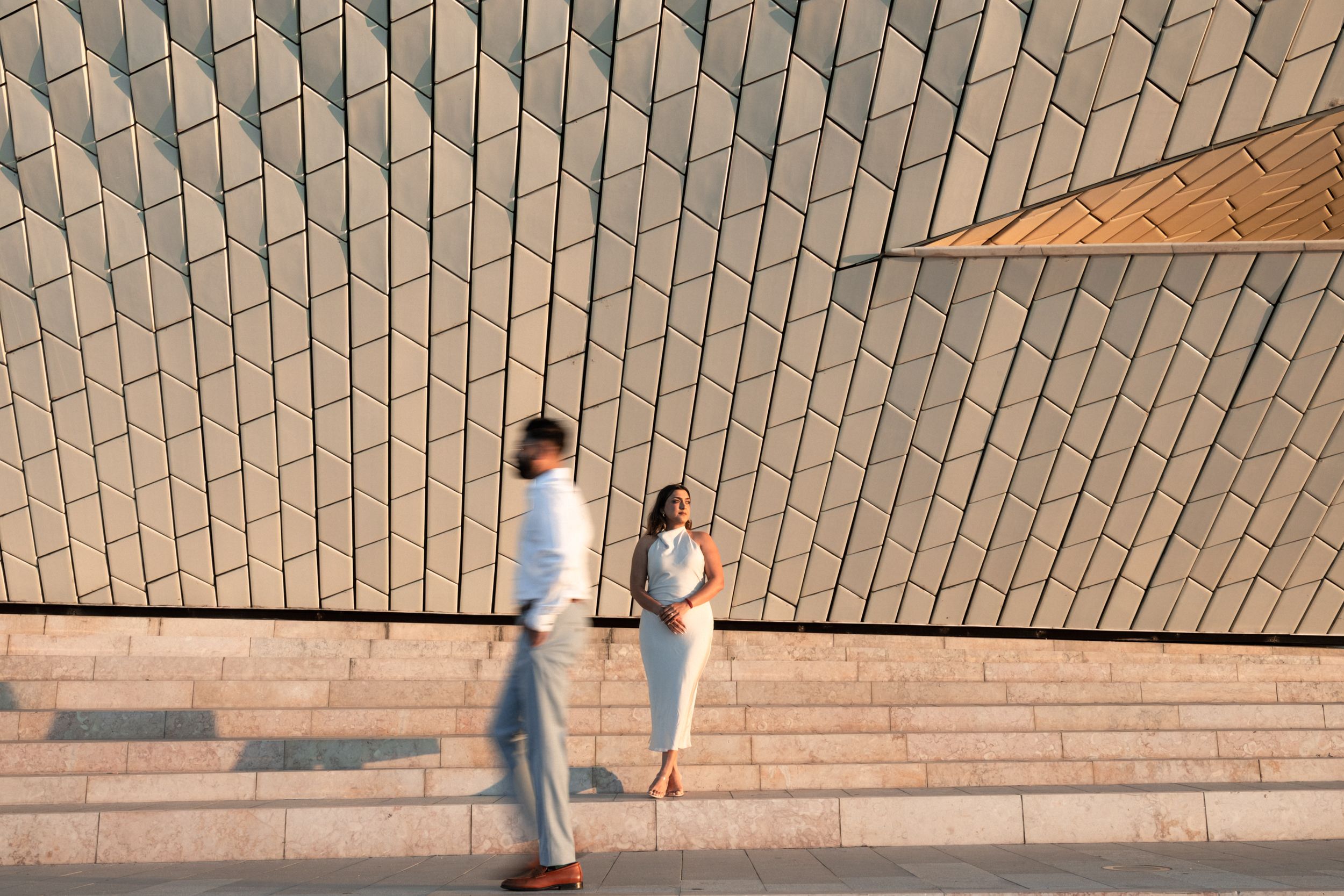 Creative engagement photo at MAAT Lisbon — bride standing still as groom walks past, modern and artistic composition. Portugal Wedding Photo