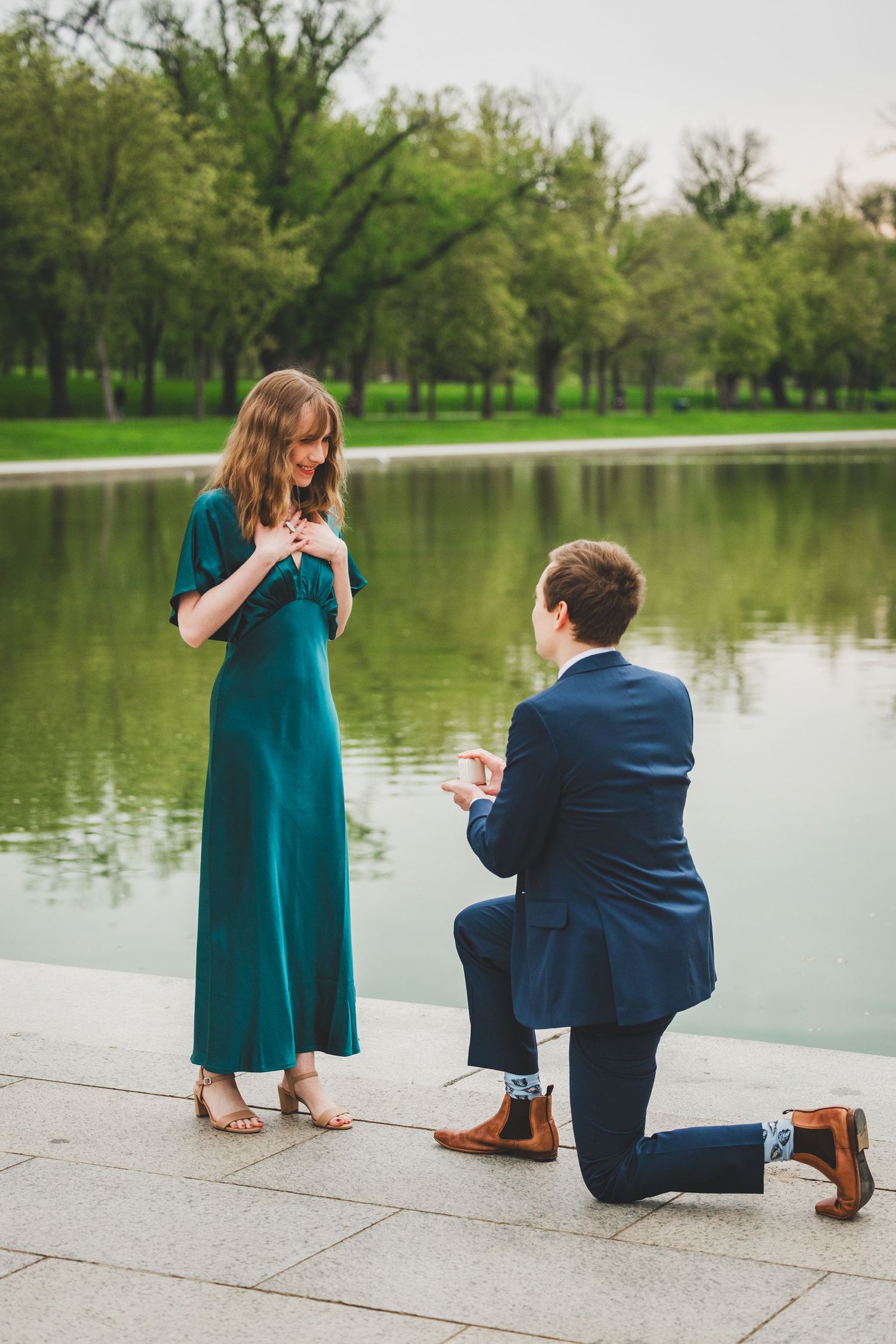 A couple shares a romantic lakeside proposal moment near the reflecting pool in washington dc