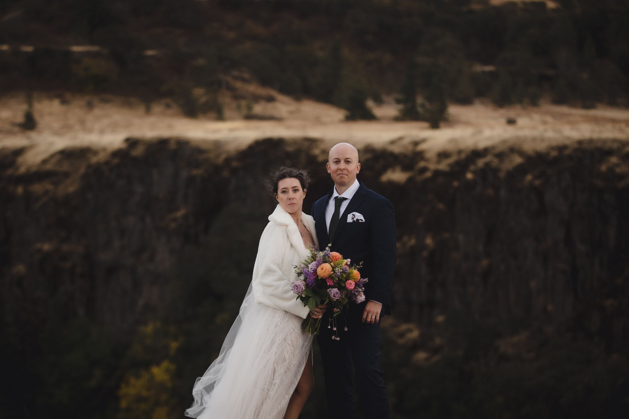 Couple in formal attire standing together against a scenic mountain backdrop at dusk.