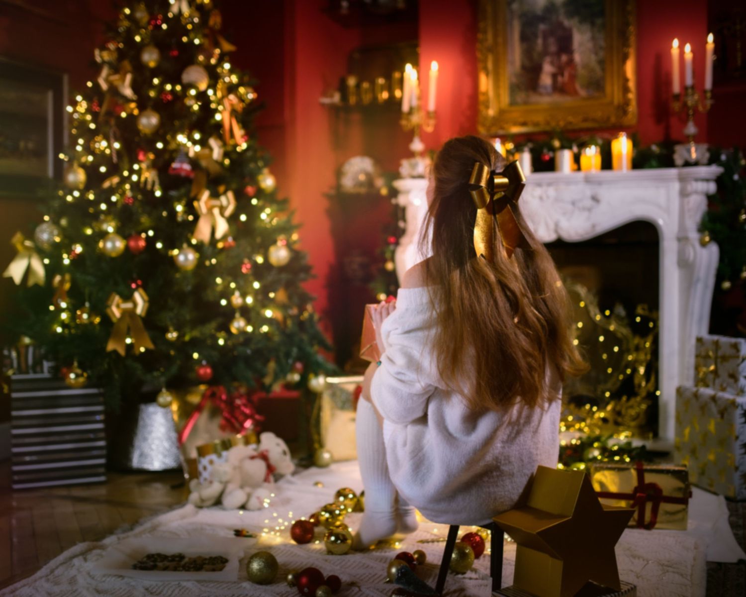 A cozy holiday scene with a Christmas tree, twinkling lights, and someone in a white sweater sitting near decorations.