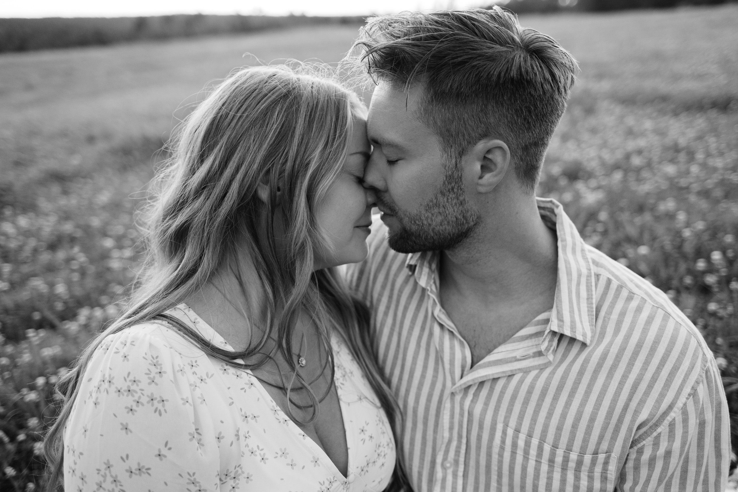 Parfotografering med Martina och Sebastian i Borgvik utanför Karlstad. Sitter på en filt tillsammans på ängen. Lutar in mot varandra. S/V.