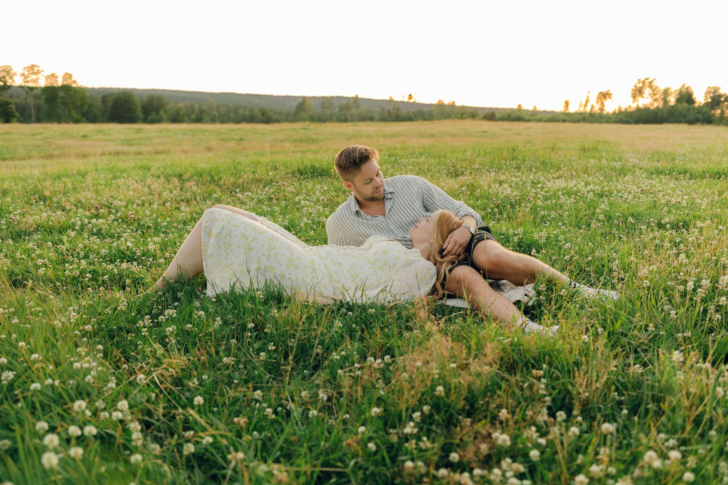 Parfotografering med Martina och Sebastian i Borgvik utanför Karlstad. Hon ligger i hans knä på äng.